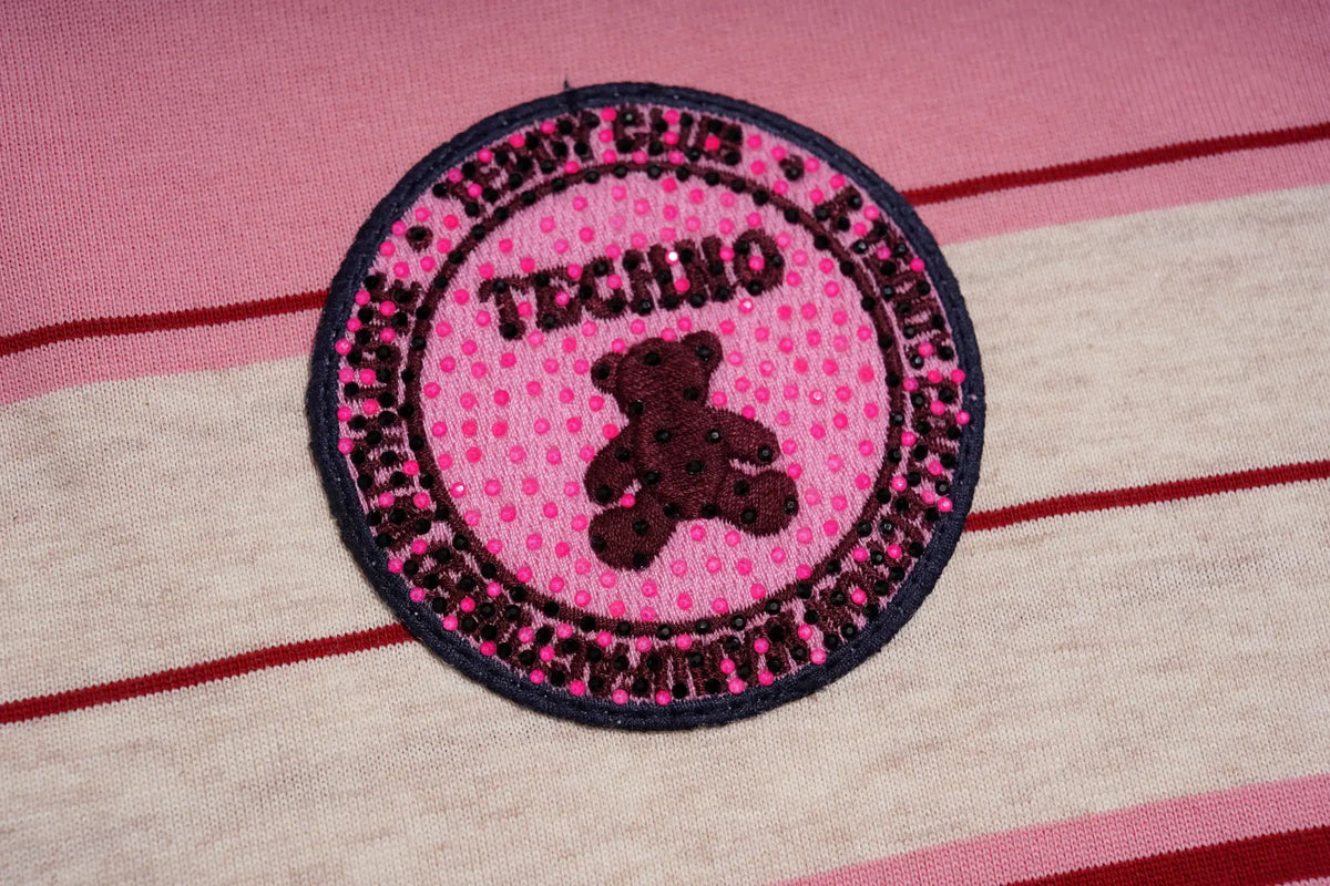 A circular embroidered patch featuring a pink polka-dot background, a dark red teddy bear in the center, and the text 'TECHIO' and 'TEENTY CLUB' around the border, shown on a pink and cream striped fabric background. TCH Women's Striped Polo Mini Dress