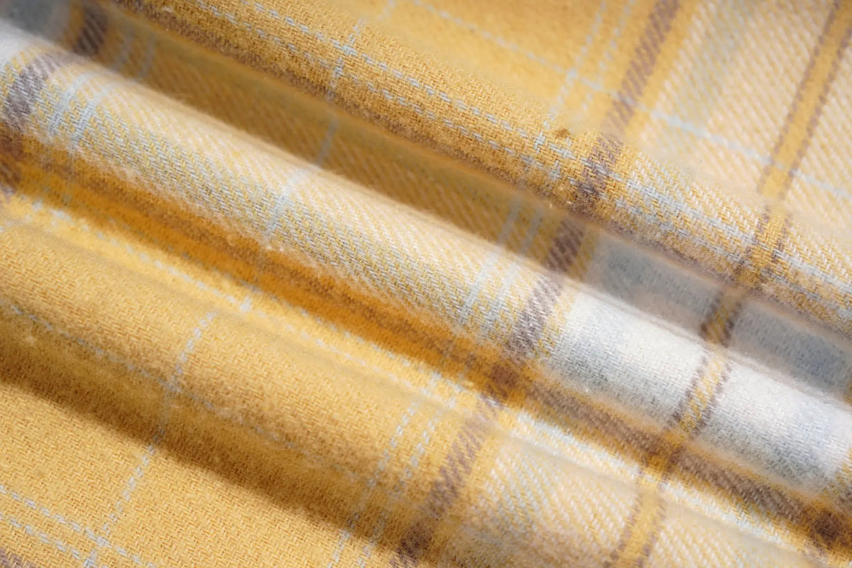 A close-up of folded yellow plaid fabric with white and gray stripes, showing the woven texture and pattern details. TCH Yellow Plaid Embroidered Cross Shirt