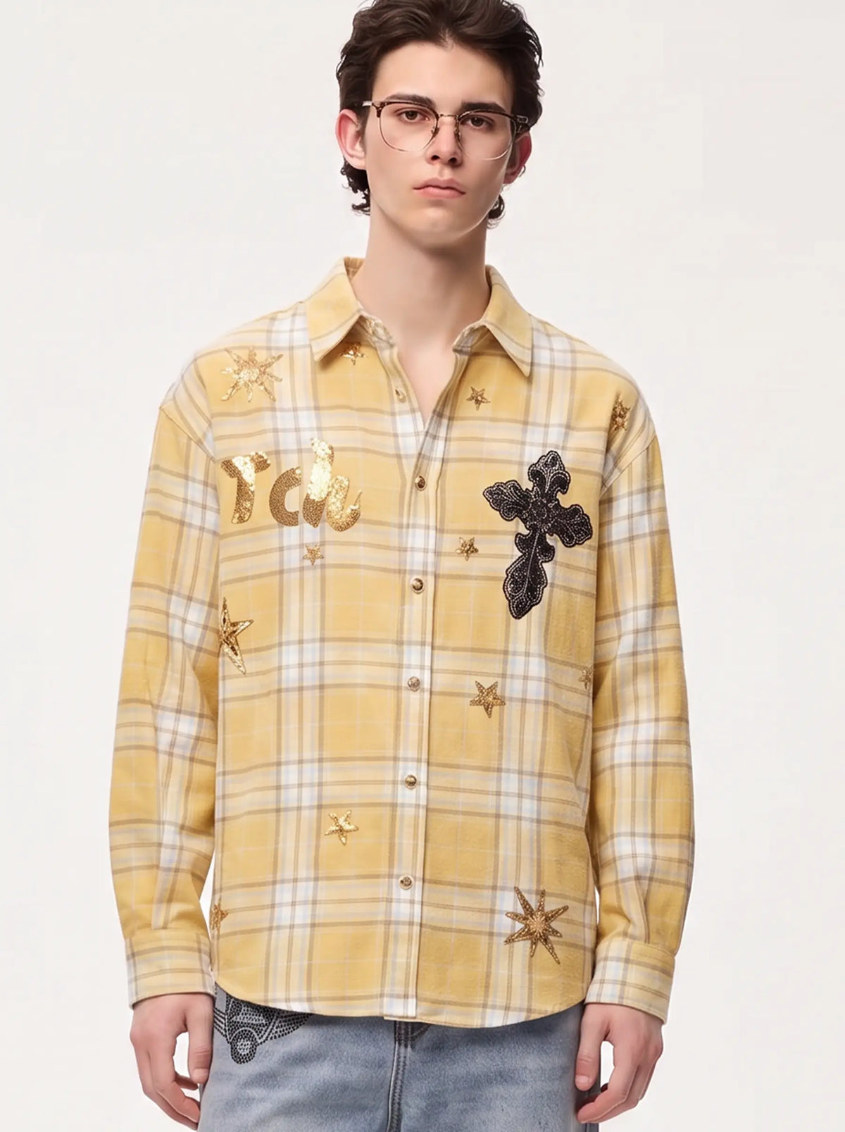 A model wearing a light blue denim jacket with various embroidered patches, including a teddy bear on the left chest and cherries on the sleeve, styled over a white t-shirt and dark pants. TCH Yellow Plaid Embroidered Cross Shirt