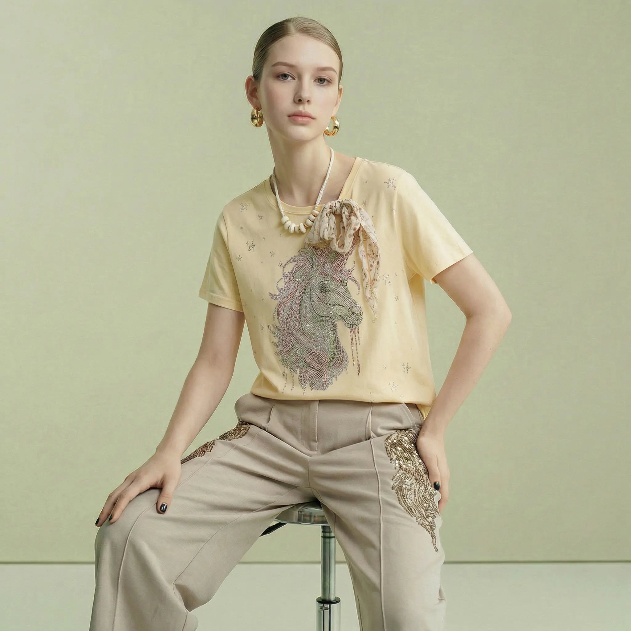 Woman wearing a yellow embroidered top and beige pants on a light green background, TCH Yellow Rhinestone Realistic Unicorn Graphic Bow Detail T-Shirt