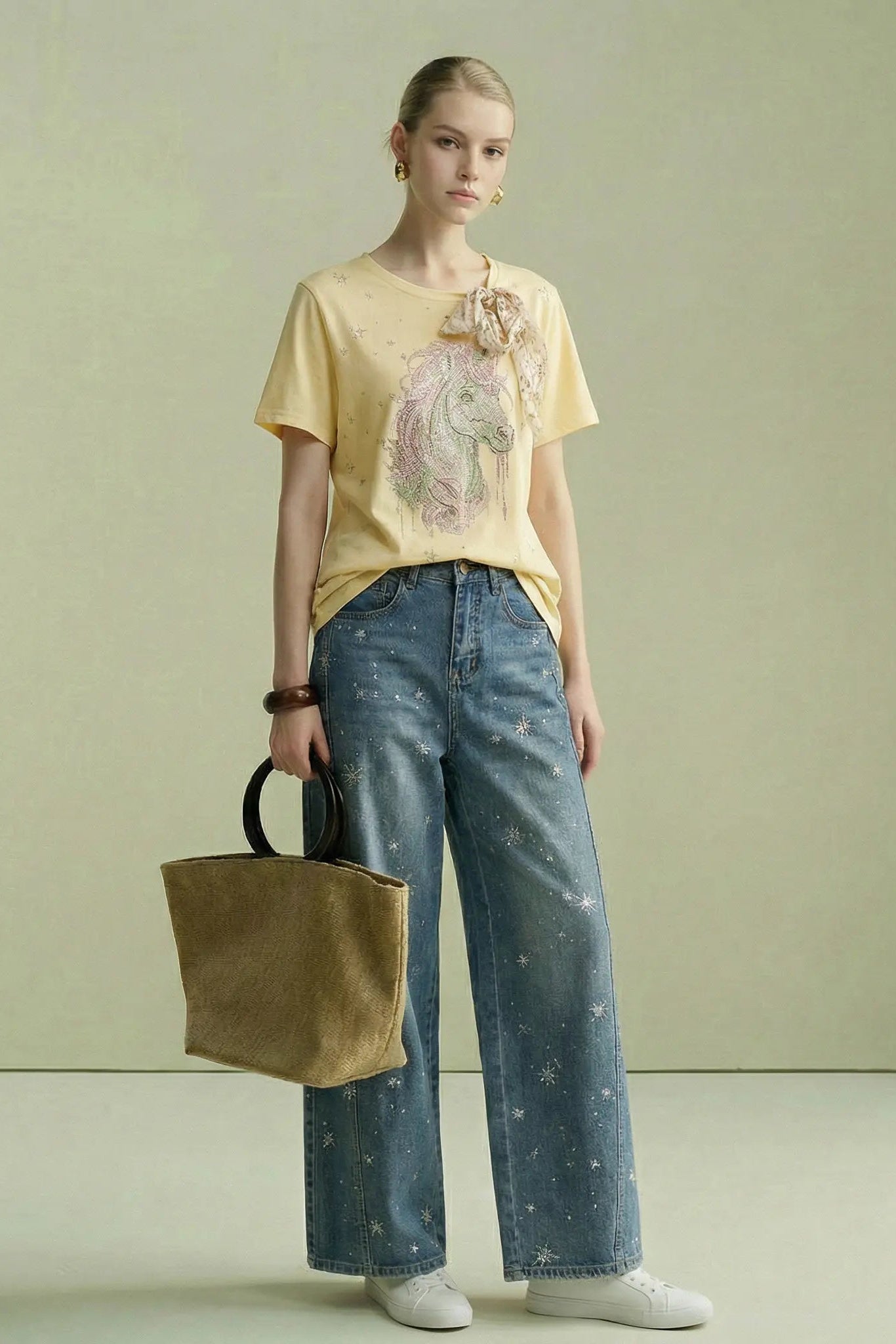 Woman wearing a yellow t-shirt with a graphic design and blue jeans, holding a brown bag against a light green background. TCH Yellow Rhinestone Realistic Unicorn Graphic Bow Detail T-Shirt