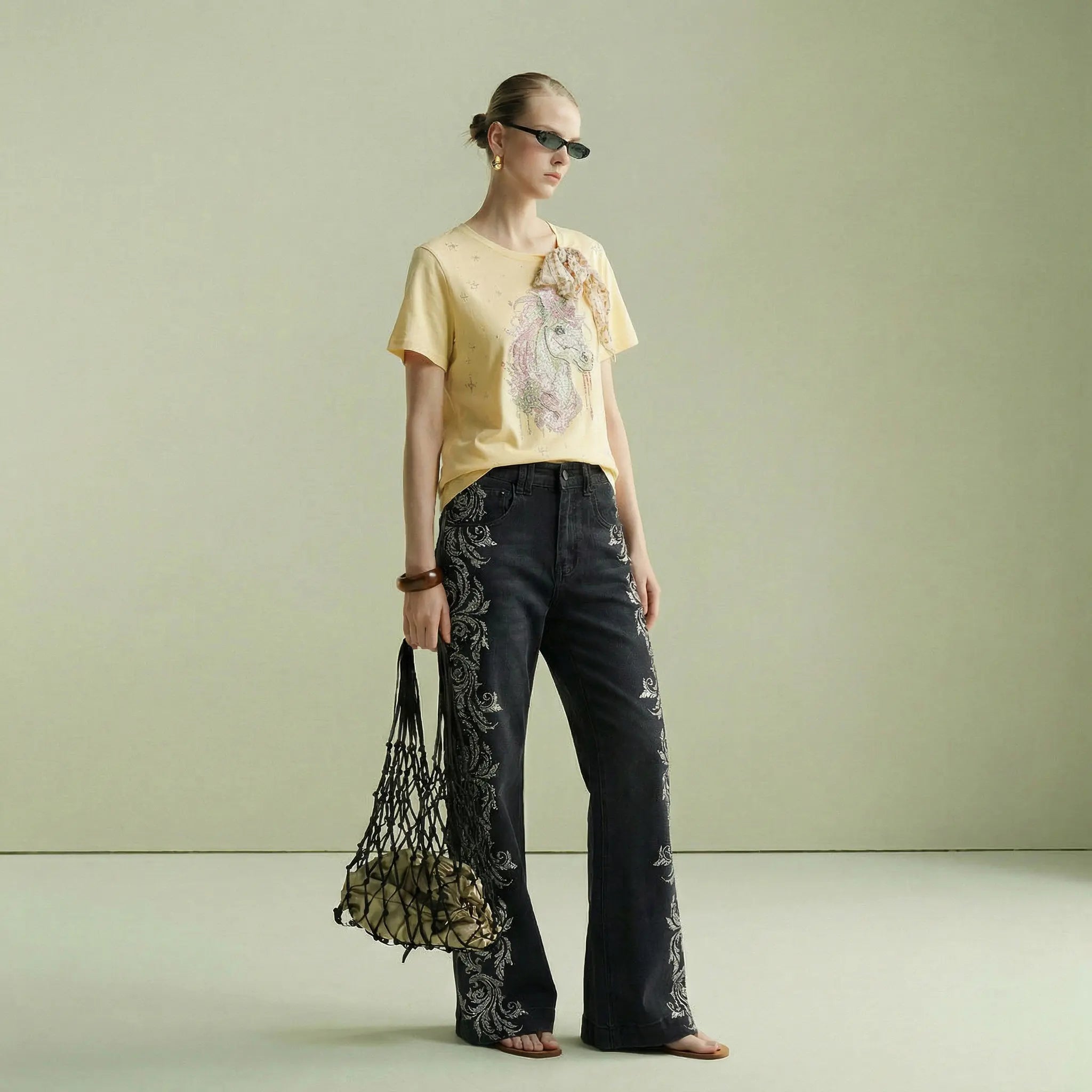 Woman wearing a yellow top and black pants with floral patterns, holding a netted bag. TCH Yellow Rhinestone Realistic Unicorn Graphic Bow Detail T-Shirt