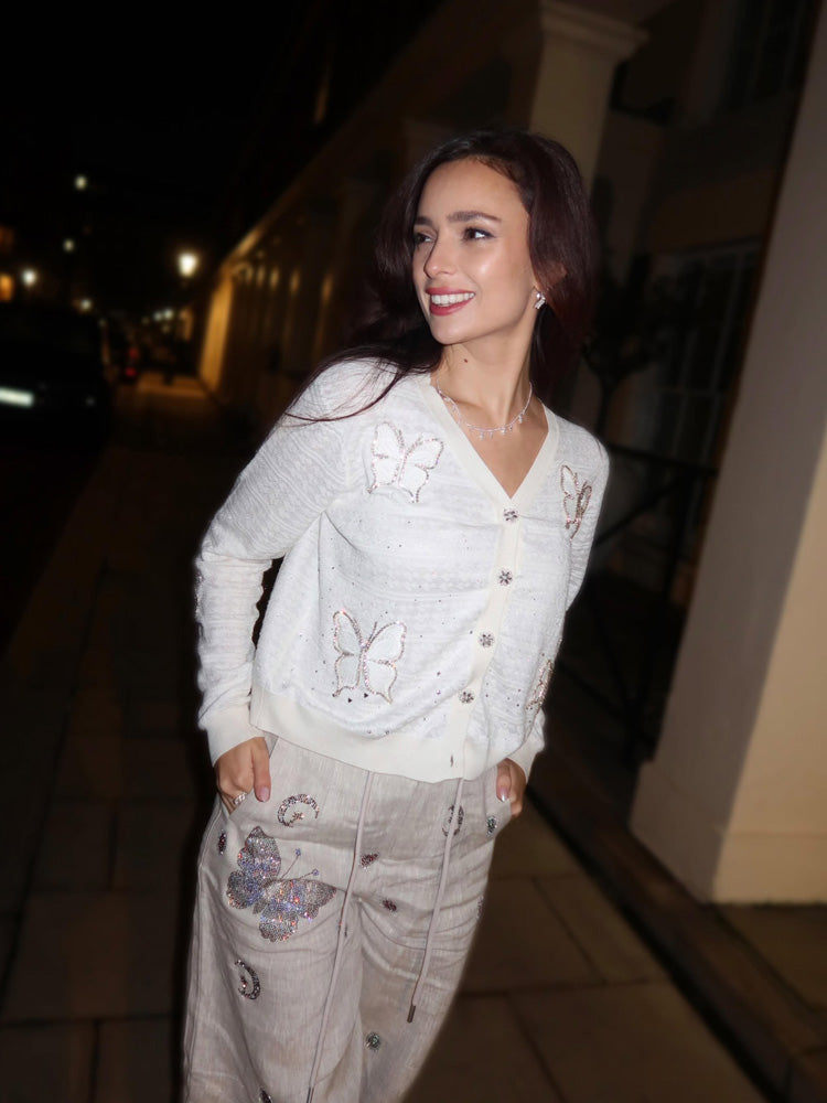 Woman wearing a white sweater with butterfly patterns outdoors at night.