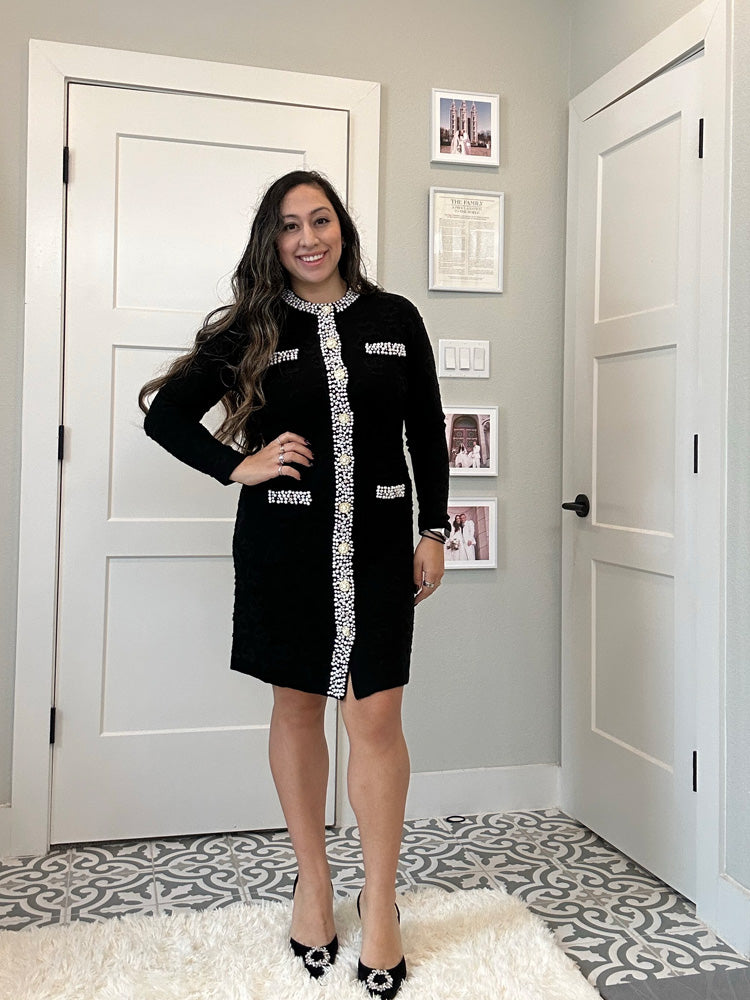 Woman wearing a black dress with white embellishments in a room with white doors and decorative floor.