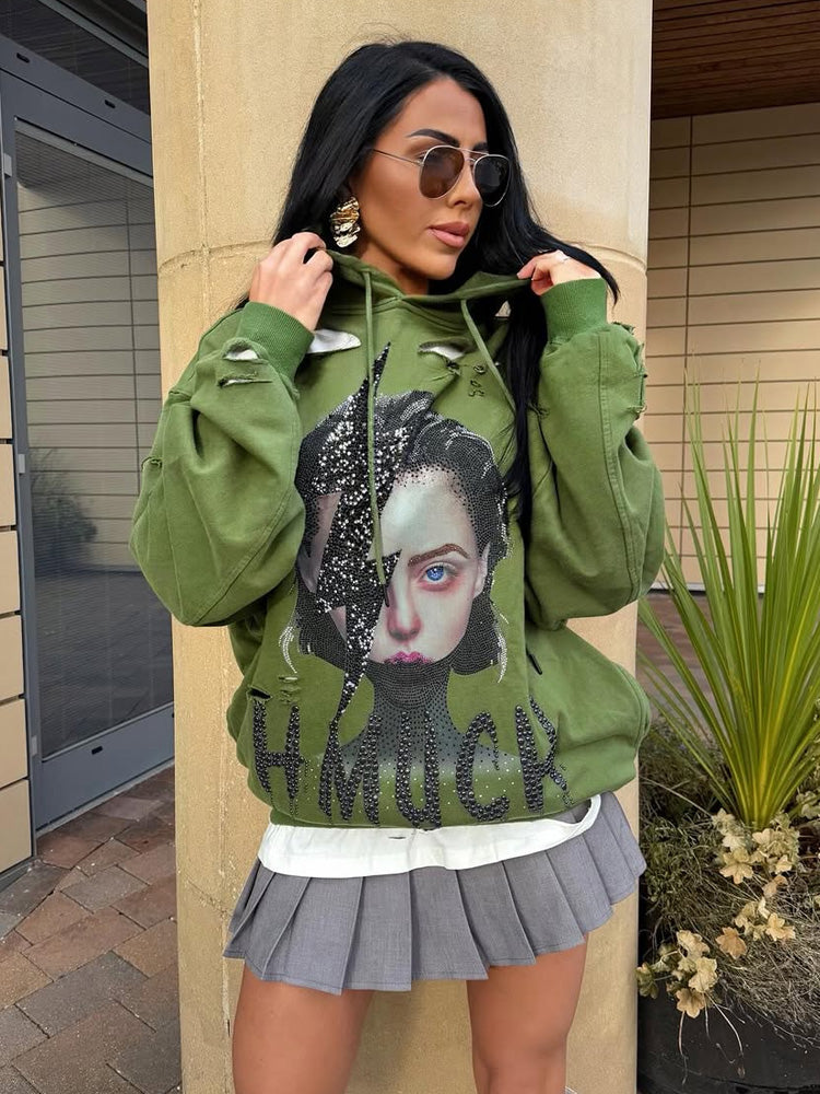 Woman wearing a green hoodie with graphic design and text, standing outdoors.